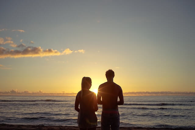 a couple staring down a sunset at the beach.