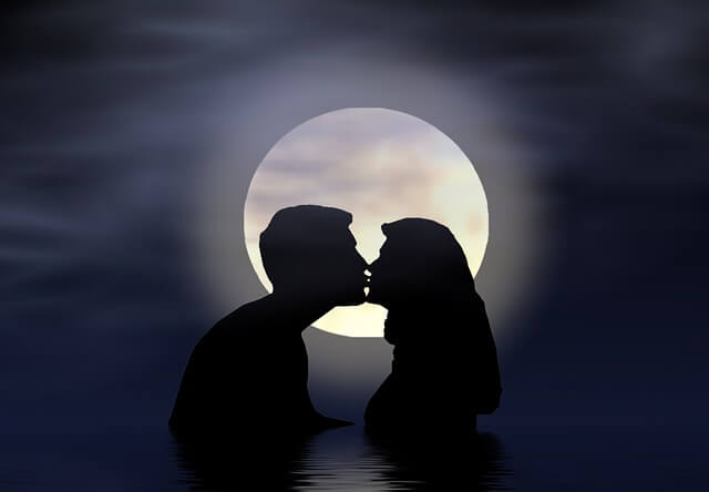 man and a woman kissing in front of the moon.